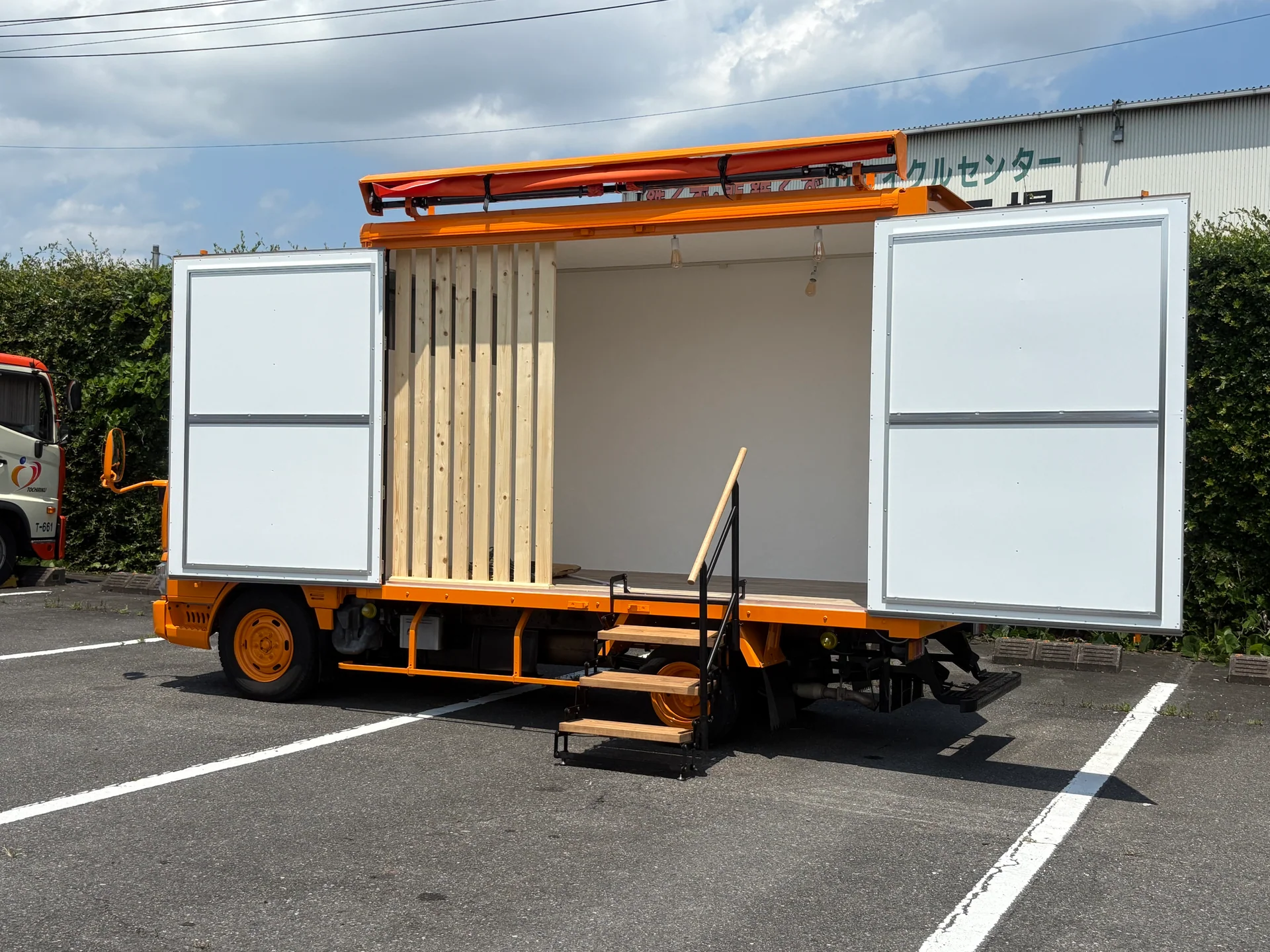 側面を開いたオレンジと白の販売車両